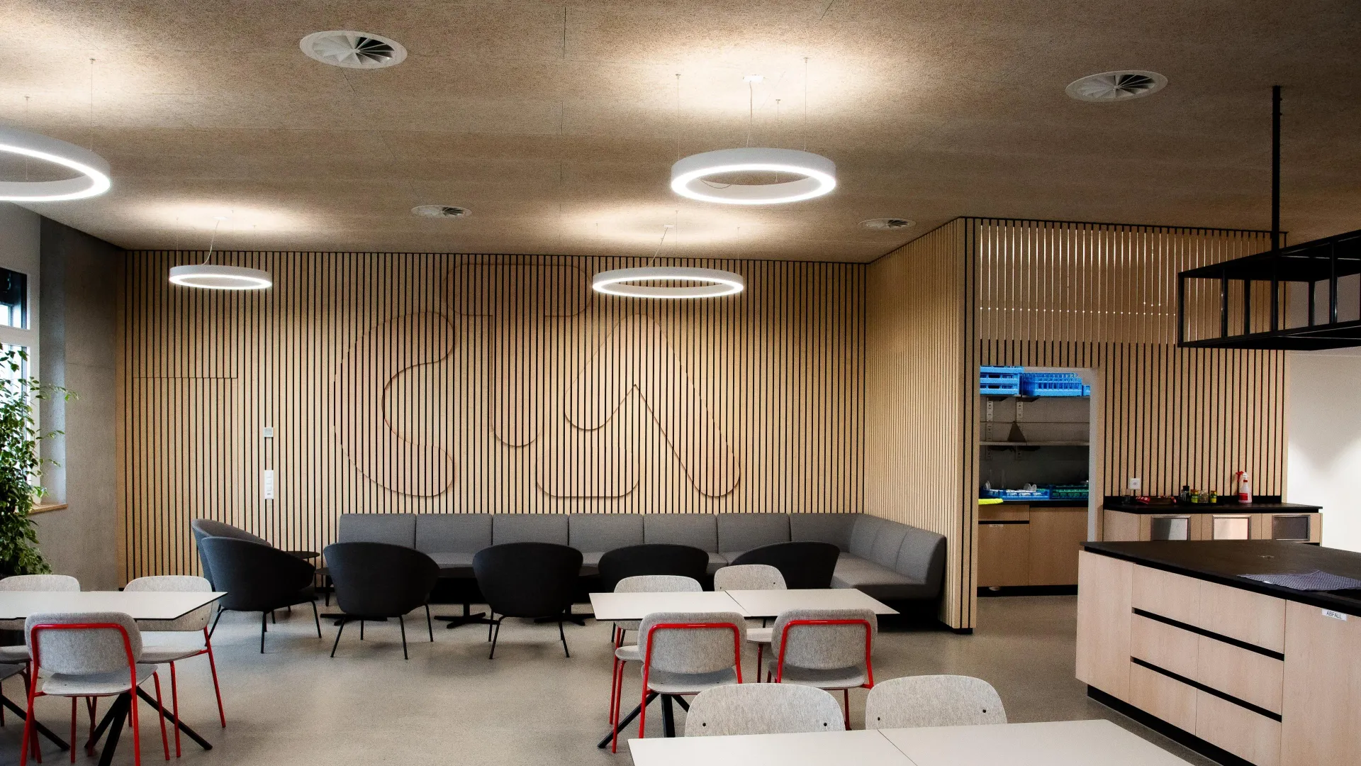 Contemporary office breakroom with wood slat walls, circular pendant lights, and mixed seating.