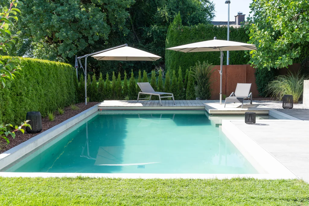 Modern outdoor pool with turquoise water, lounge chairs, and parasols in a landscaped garden.