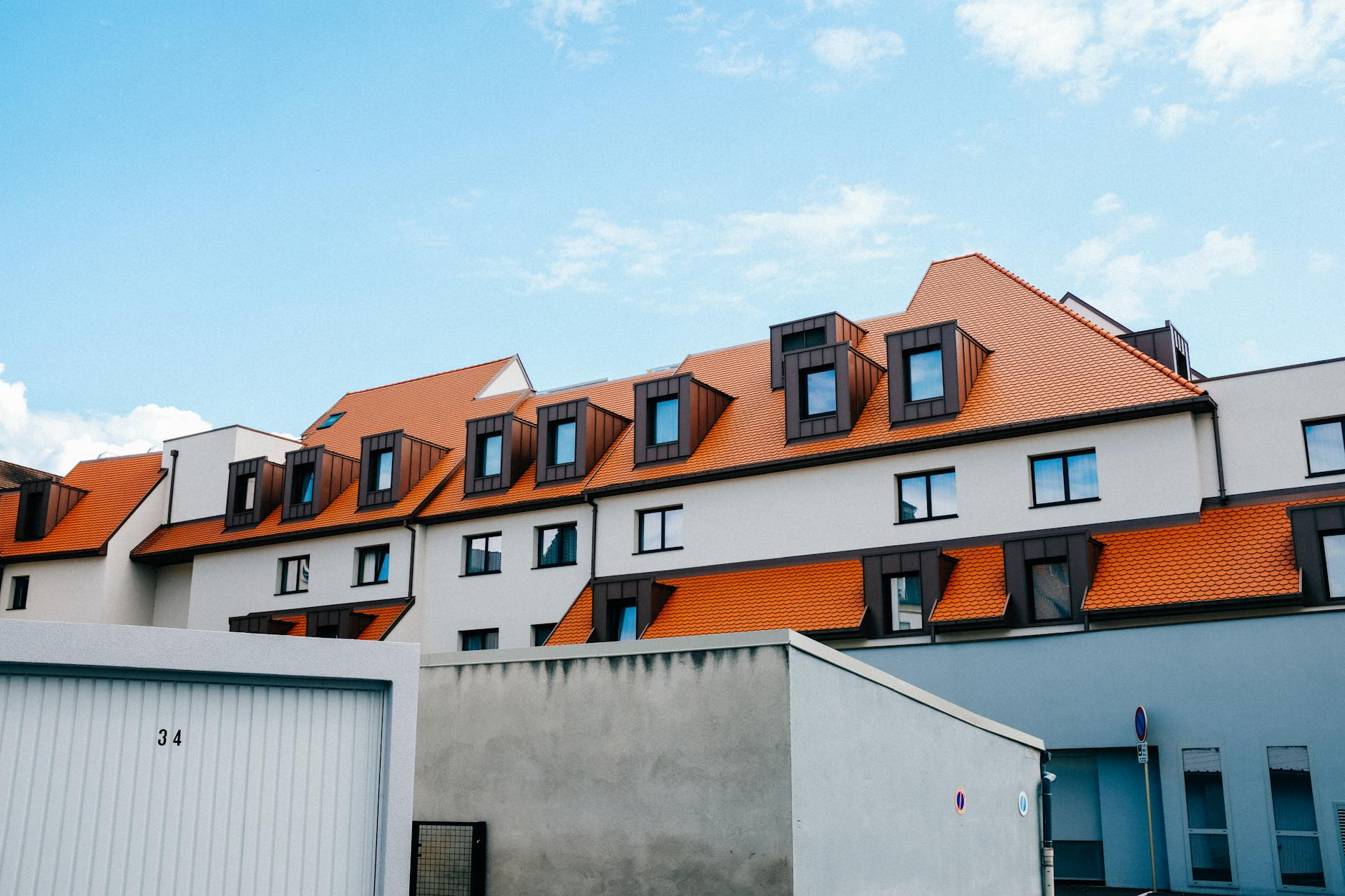 Ein Schweizer Dachgeschosszimmer mit schrägen Decken, in das warmes Sonnenlicht durch ein grosses Fenster fällt, während eine einfache Klimaanlage und geschlossene Aussenjalousien für Kühlung sorgen.