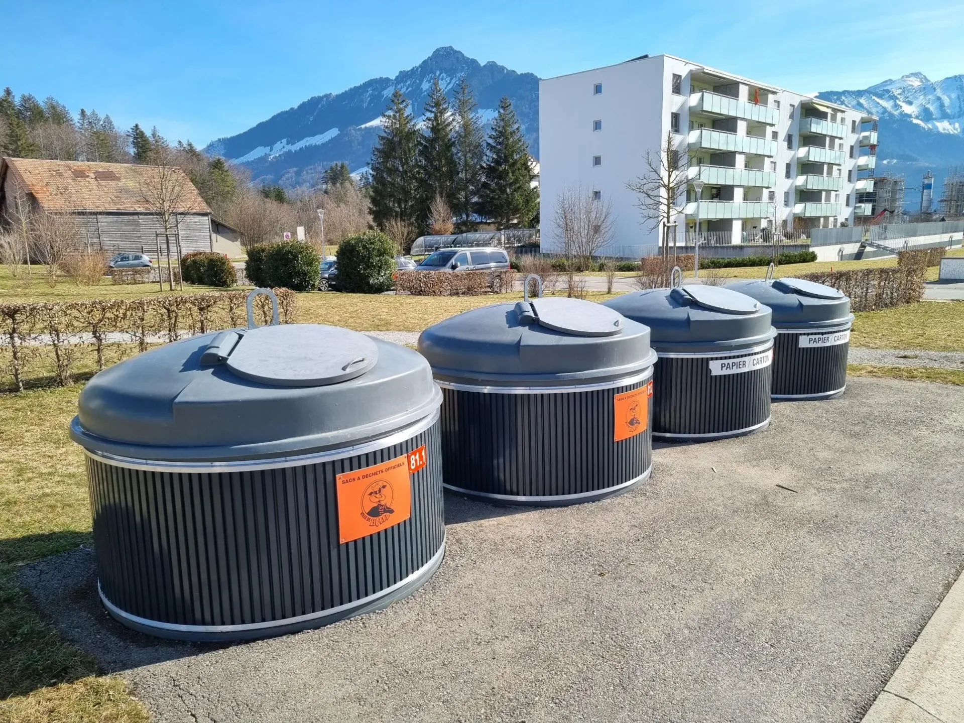 Three stainless steel semi-underground waste collection containers labelled for paper and general waste in a residential area.