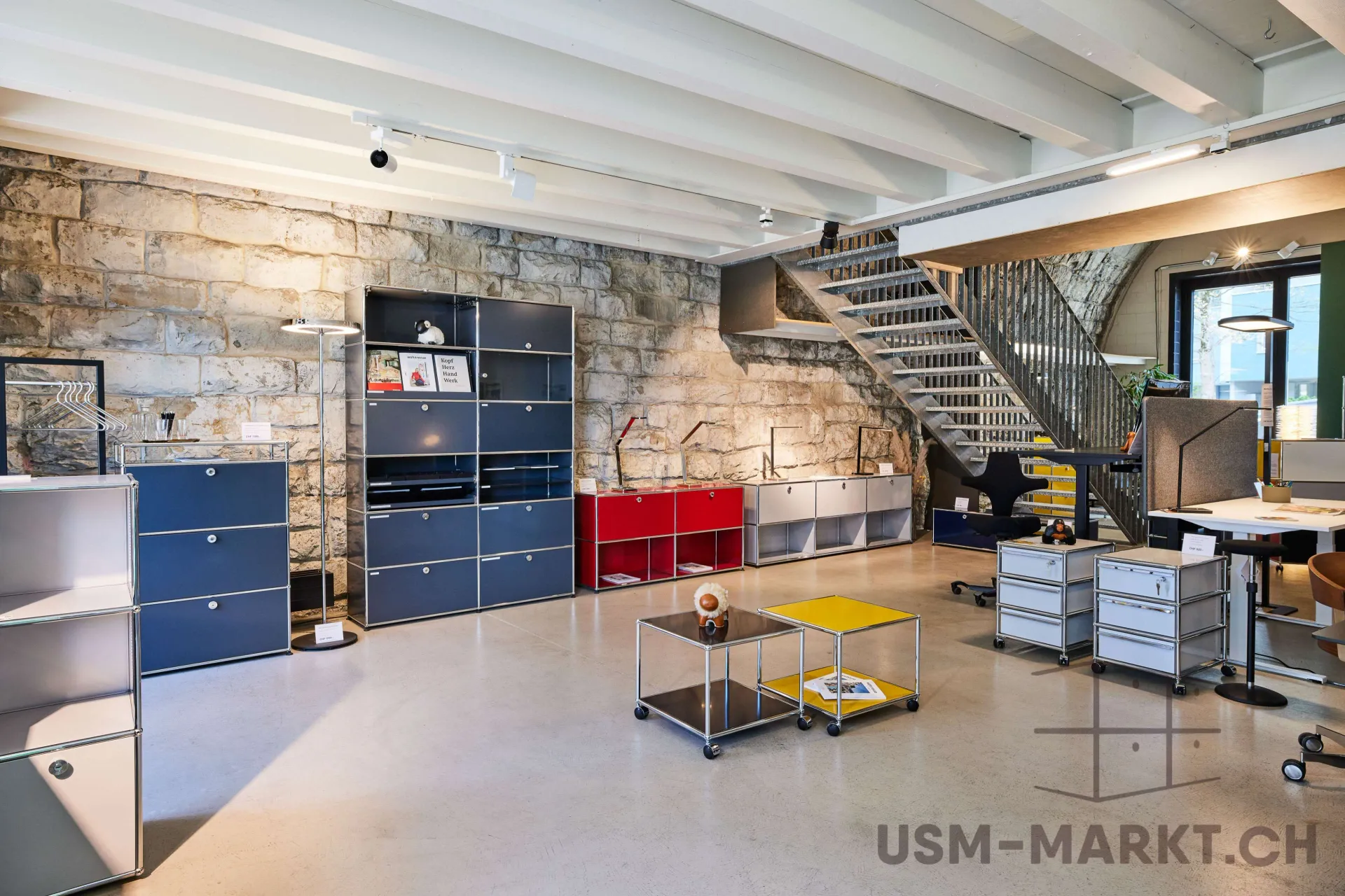 Bright showroom displaying USM modular furniture in various colors with ergonomic chairs and height-adjustable desks.
