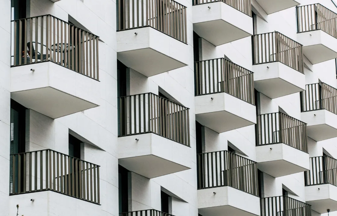 Ein Schweizer Wohnungsbalkon mit architektonischen Plänen und einem Massband, das Bauvorschriften und Genehmigungsprozesse für Balkonumbauten symbolisiert