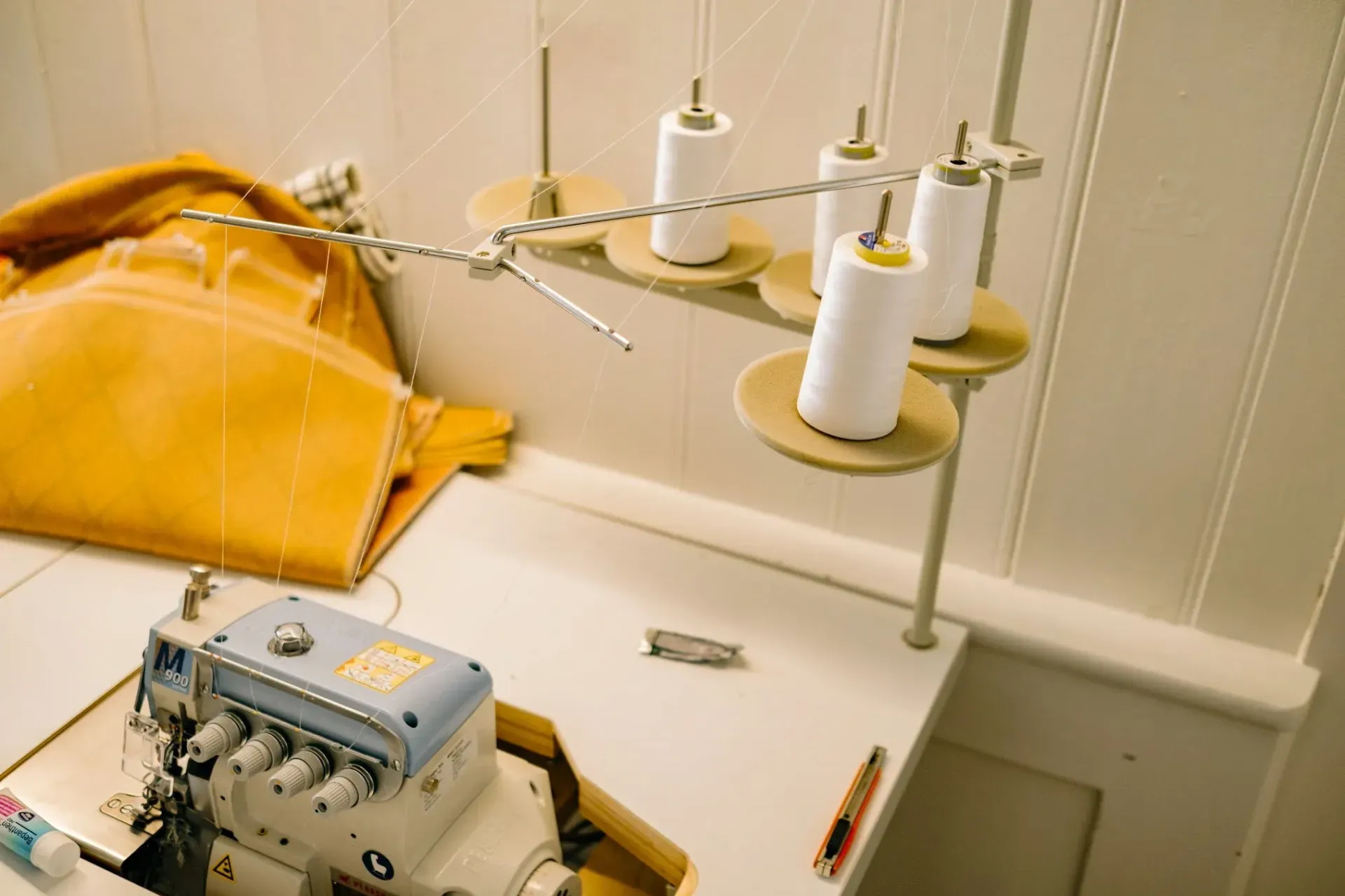 Smiling upholsterer holds thread while working on patterned fabric in a bright workshop.