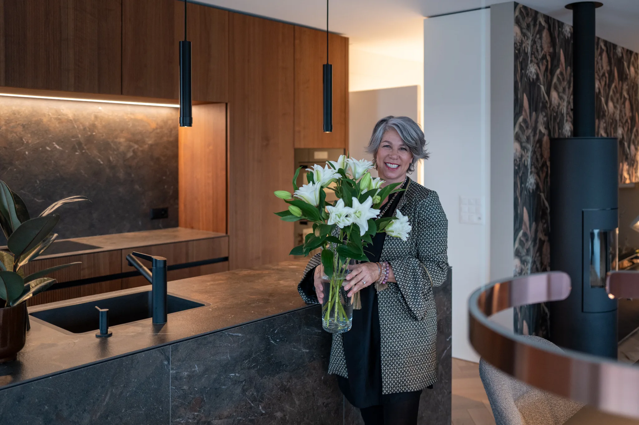 Karin Decurtins smiling while arranging a woven pendant lamp on a terrace, showing her hands-on passion for decorative details and personal design philosophy.