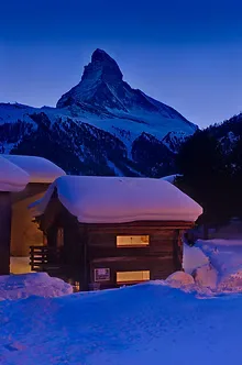 Snow-covered chalet beneath the iconic Matterhorn at twilight, perfectly evoking Zermatt's magical winter atmosphere described in the article.