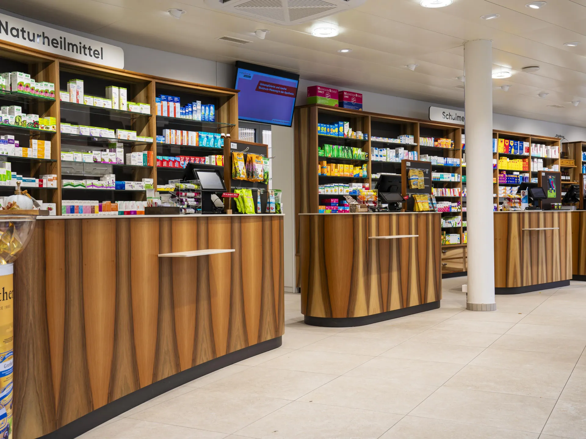 Pharmacy counter area with decorative wood-grain laminate fronts and fully stocked shelving behind.