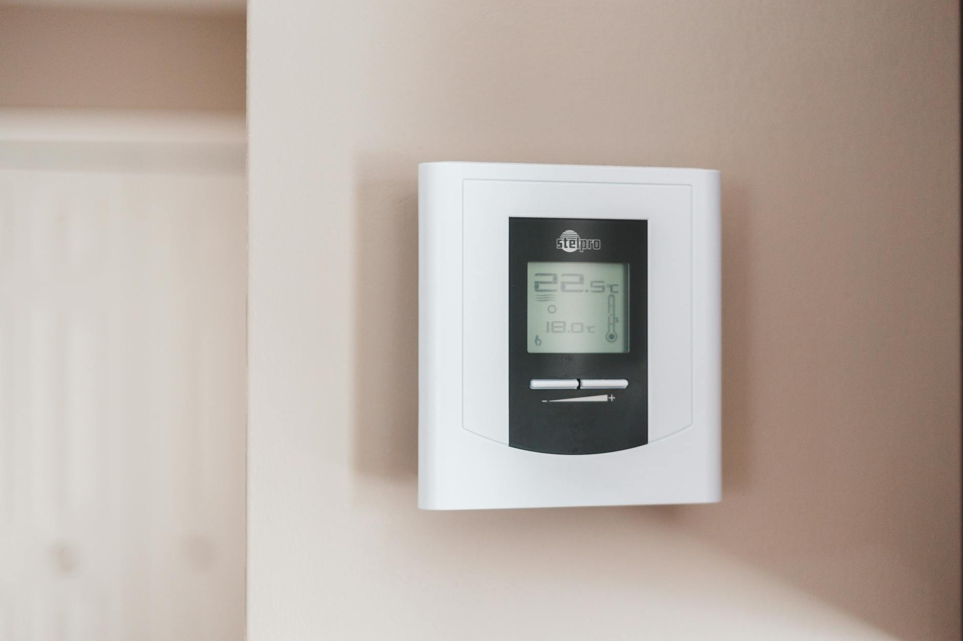 Moderne Schweizer Wohnung mit diskret integrierter Smart-Home-Technologie: Ein helles Wohnzimmer mit Smart-Thermostat an der Wand, Steuerungspanel und energiesparender Beleuchtung.