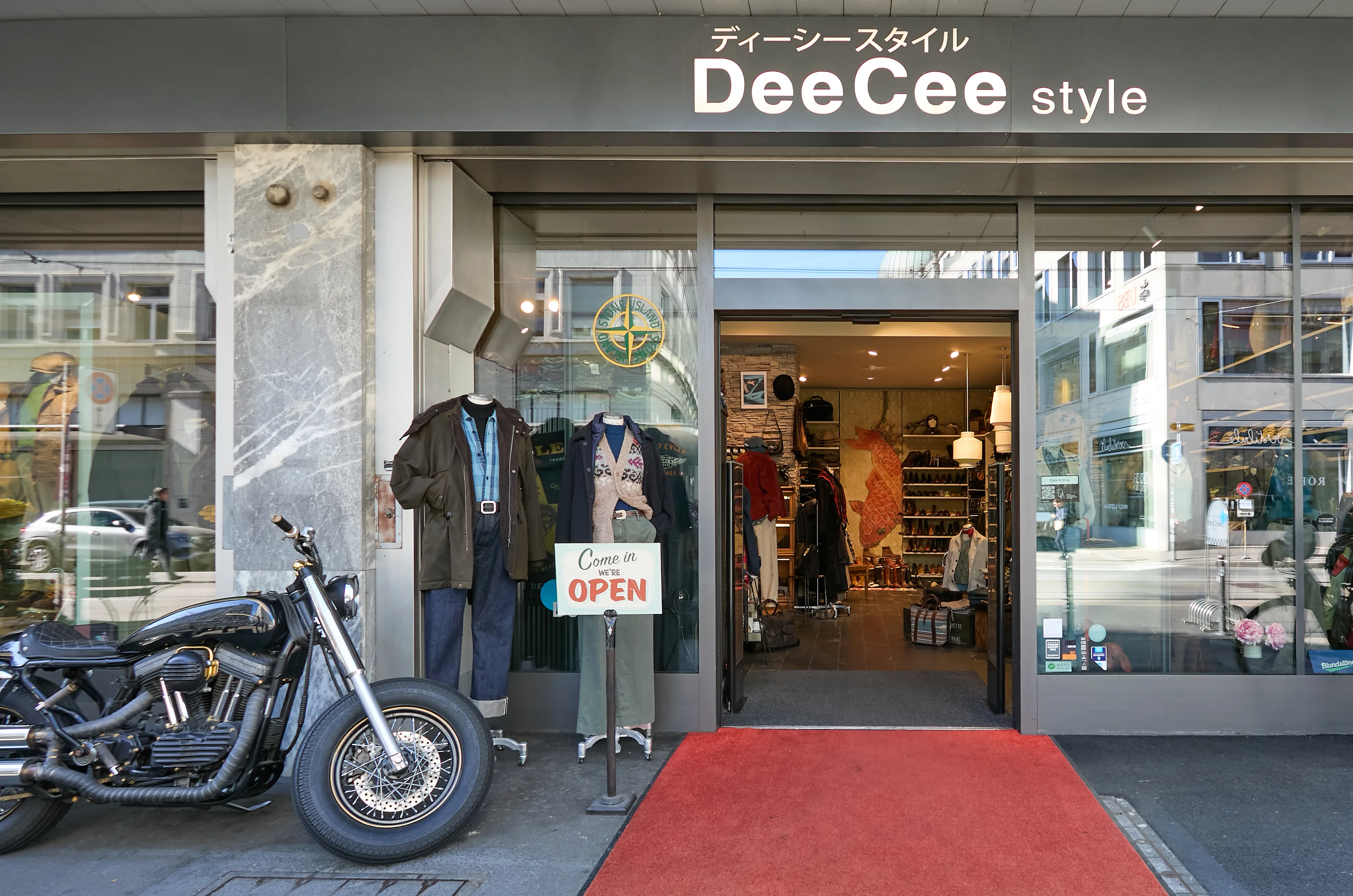 The DeeCee style storefront with a classic motorcycle parked on a red carpet outside.