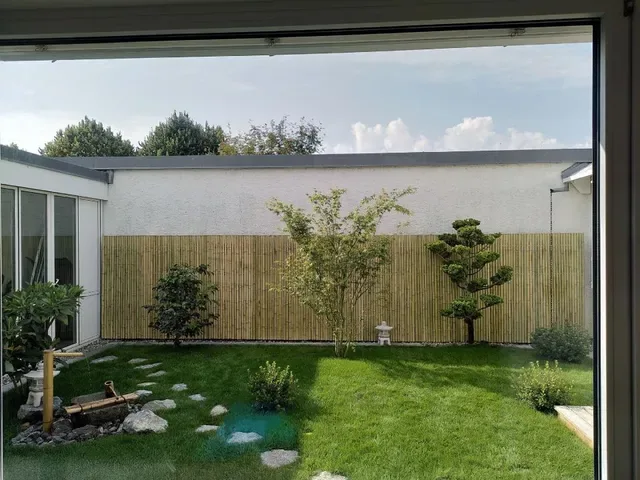 View through glass doors into a Japanese inner garden with cloud-pruned trees and stone lanterns.