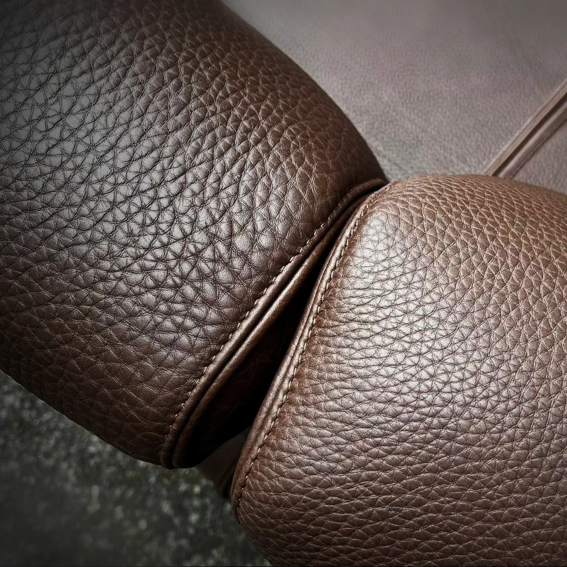 Close-up of two-tone brown pebbled leather cushions meeting with precise stitching on a sofa.
