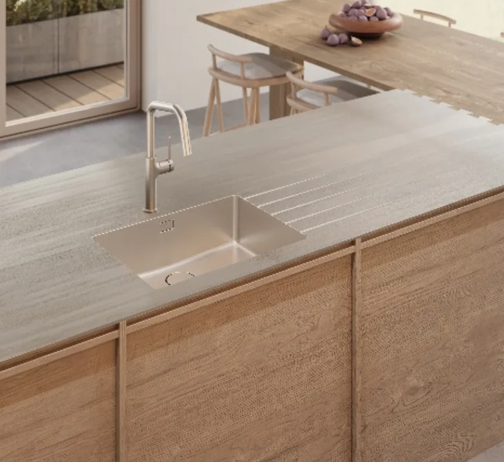 Sleek stainless steel kitchen island with integrated sink and curved faucet against light wood cabinetry.