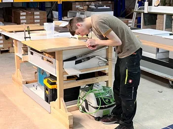 Young craftsman working attentively at a wooden workbench in a professional kitchen workshop.