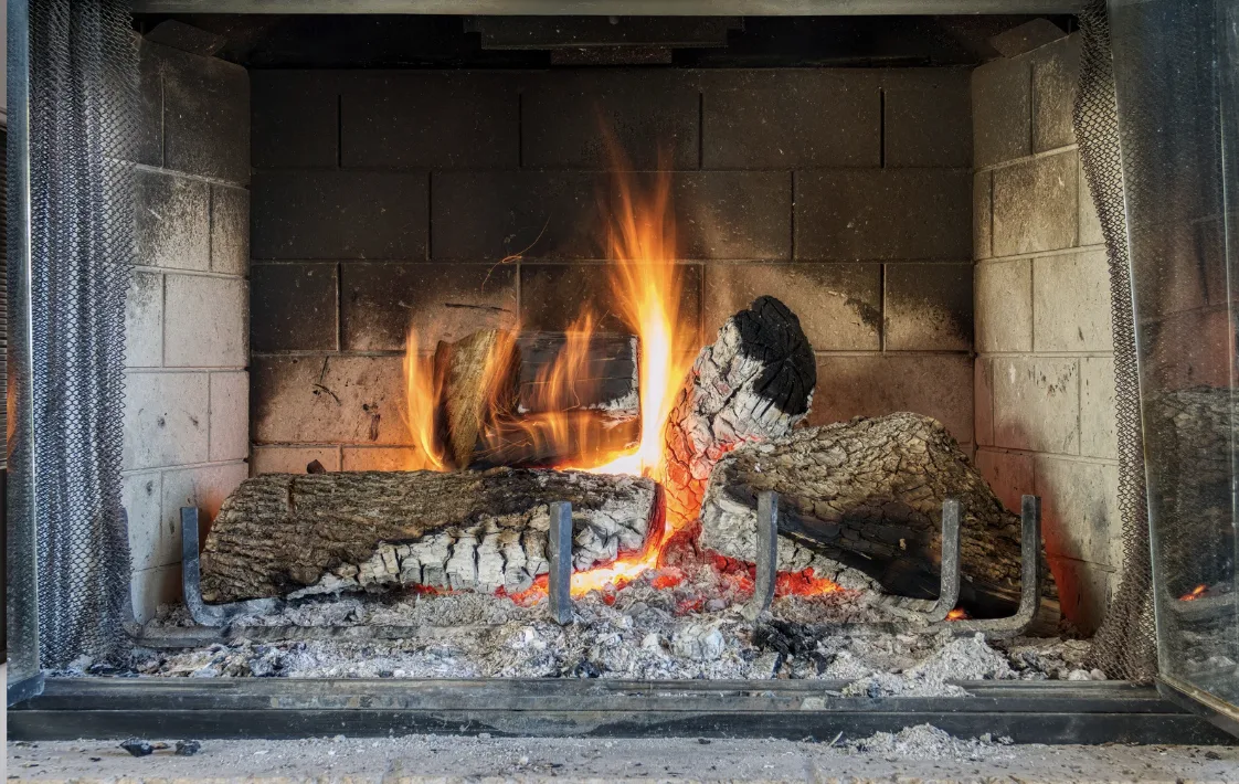 Ein moderner Holzofen in einer schweizerischen Wohnstube mit trockenem Brennholz daneben, symbolisiert umweltfreundliches und gesetzeskonformes Heizen.