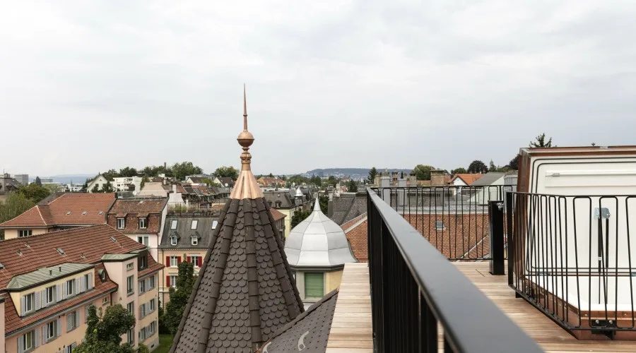 Rooftop terrace with wooden decking overlooking historic town rooftops and a copper-spired tower.