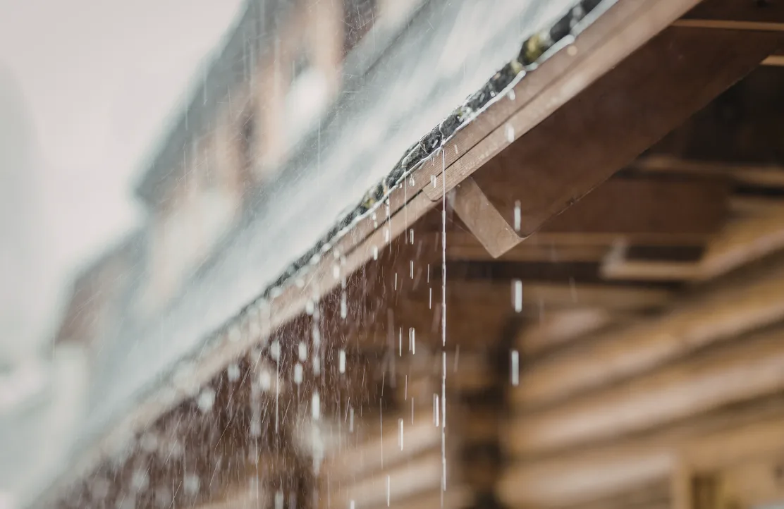 Eine moderne Schweizer Einfamilienhausfassade mit Regenrinne, die in eine grosse Regentonne im Garten führt, um Regenwasser für die nachhaltige Bewässerung zu sammeln.