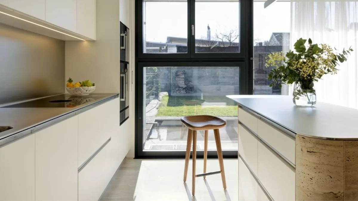 Sleek modern white kitchen with island, garden view, and natural light flooding the space.