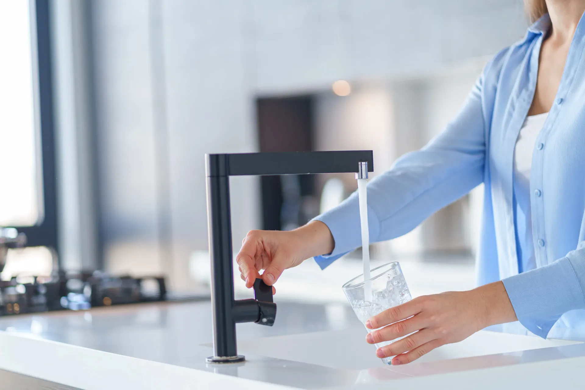 Woman filling a glass of water at a sleek black kitchen faucet perfectly illustrates water as a source of everyday freshness.
