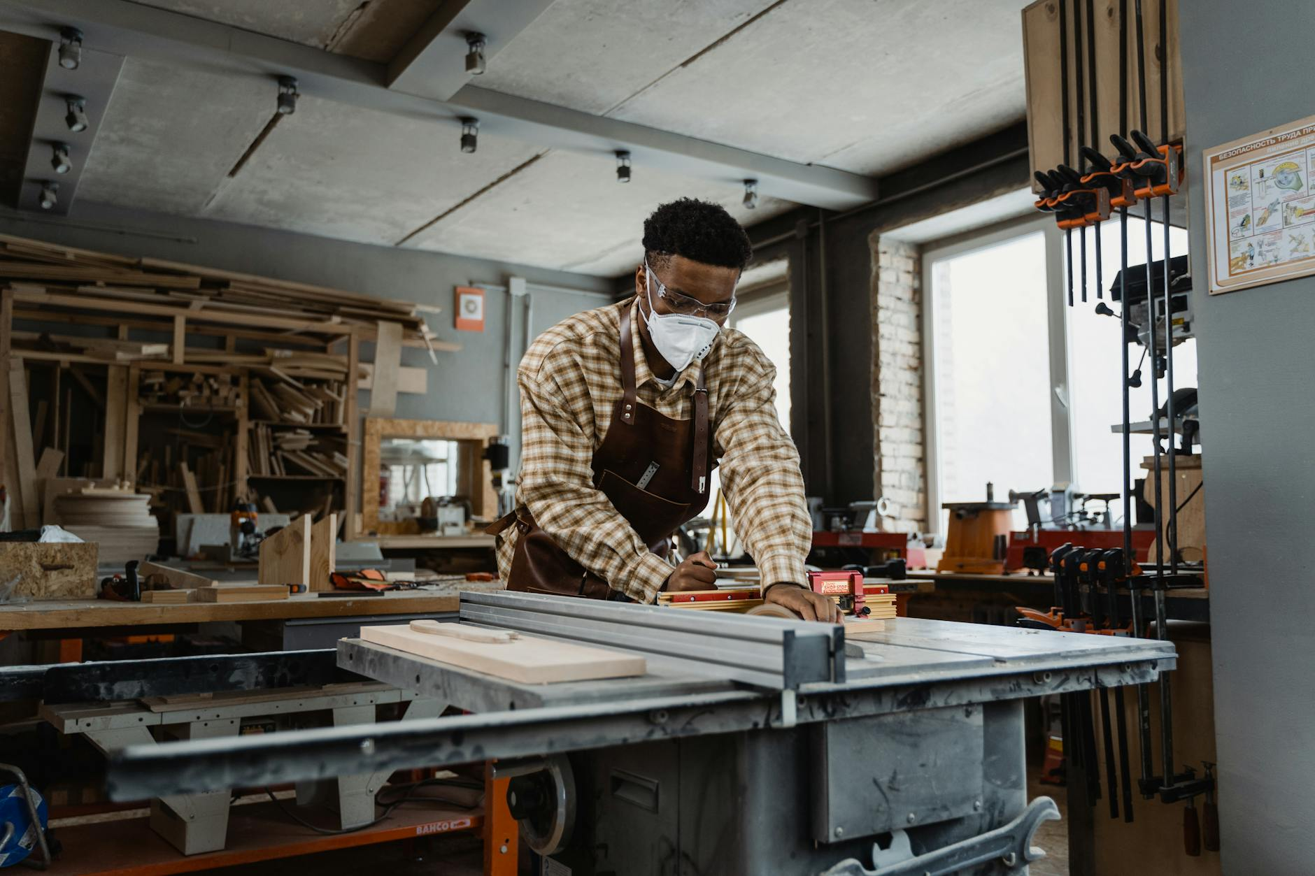 Ein Schweizer Schreiner arbeitet an einem massgefertigten Eichentisch in einer hellen Werkstatt, während daneben moderne Serienmöbel aus Schweizer Produktion zu sehen sind.