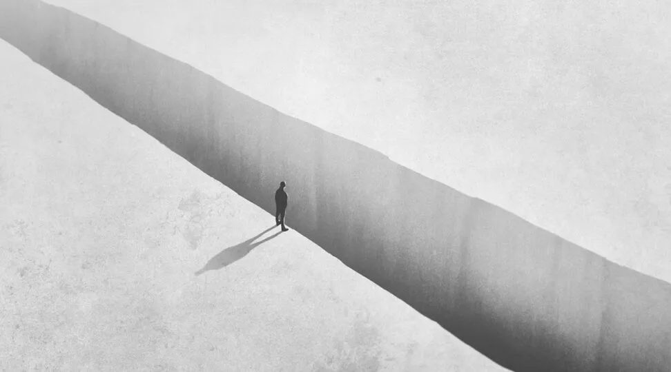 Lone figure standing at the edge of a deep crack in a vast white landscape.