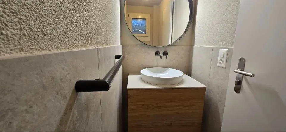 Elegant attic bathroom with freestanding tub, wood vanity, round LED mirror, and warm ambient lighting.