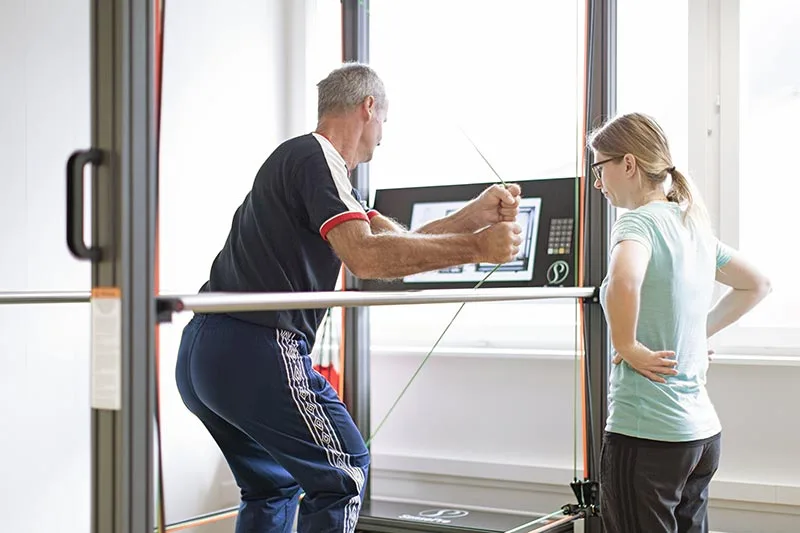 A physiotherapist guides a patient through a cable-machine exercise, showing the hands-on, personalized approach central to Physiowerkstatt's philosophy.