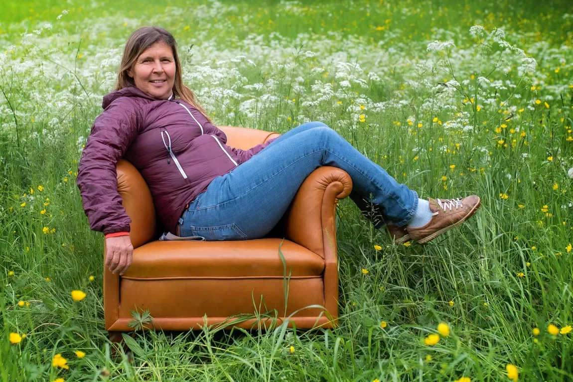 Owner Franziska Plattner relaxes confidently in a tan leather armchair set in a lush wildflower meadow.