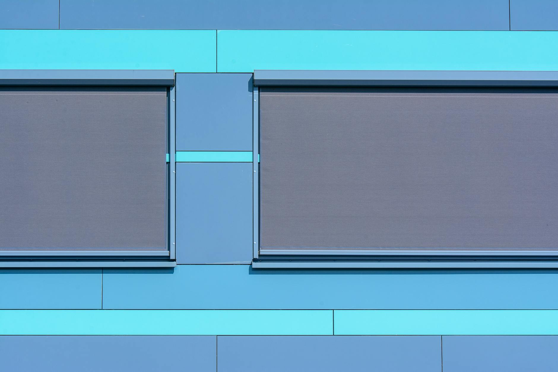 Ein Schweizer Dachgeschosszimmer mit schrägen Decken, in das warmes Sonnenlicht durch ein grosses Fenster fällt, während eine einfache Klimaanlage und geschlossene Aussenjalousien für Kühlung sorgen.